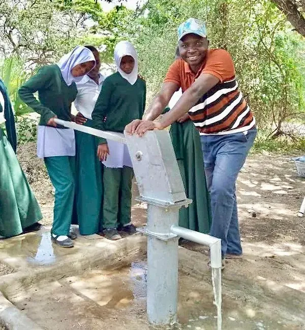 Students and a community member at a finished well, with water flowing